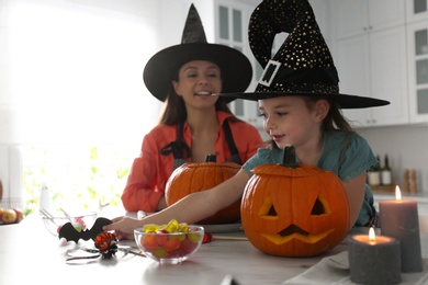 Mother and daughter making pumpkin jack o'lanterns at table in kitchen. Halloween celebration