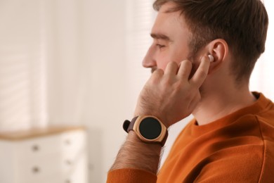 Young man with smart watch and earphones at home, space for text