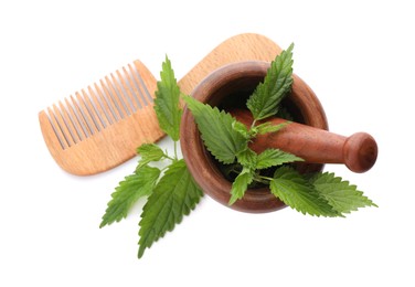 Photo of Mortar with pestle, stinging nettle and wooden comb on white background, top view. Natural hair care