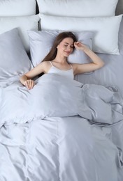 Young woman awaking in comfortable bed with silky linens, above view