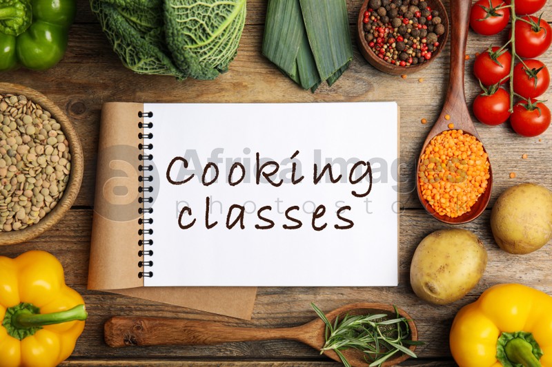 Notebook with inscription Cooking Classes and different ingredients on wooden table, flat lay