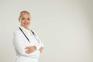 Portrait of mature doctor with stethoscope on light grey background. Space for text