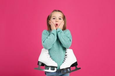 Excited little girl in turquoise knitted sweater with skates on pink background