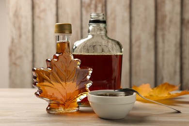 Bottles and bowl of tasty maple syrup on wooden table