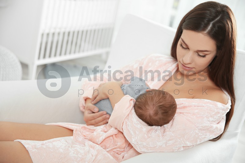 Young woman breastfeeding her baby in nursery. Space for text