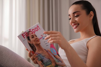 Happy young woman reading modern magazine indoors