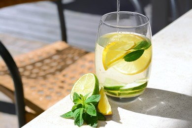 Pouring water into glass with lemon slices and mint at light grey table. Space for text