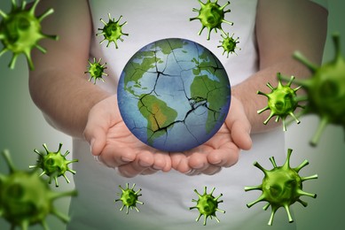 Man holding Earth with medical mask on light background, closeup. Concept of coronavirus outbreak