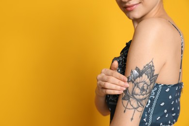 Woman applying cream onto her arm with tattoo on yellow background, closeup. Space for text