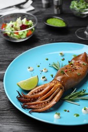 Photo of Delicious grilled squid served on black wooden table, closeup