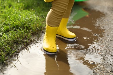 Little girl wearing rubber boots standing in puddle, closeup