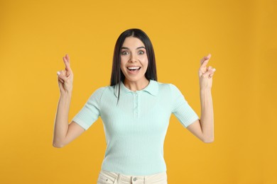 Woman with crossed fingers on yellow background. Superstition concept