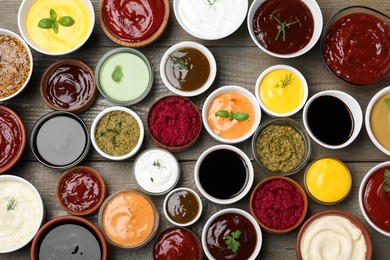 Many different sauces and herbs on wooden table, flat lay