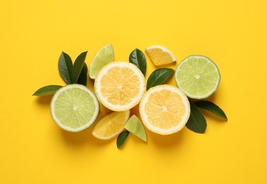 Fresh ripe lemons, limes and green leaves on yellow background, flat lay