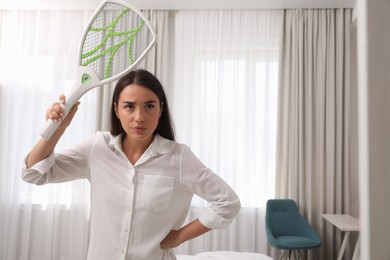 Young woman with electric fly swatter indoors. Insect killer