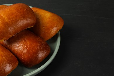 Delicious baked pirozhki on black table, closeup. Space for text
