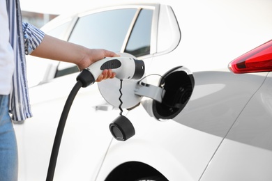 Woman inserting plug into electric car socket at charging station, closeup