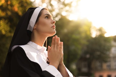 Photo of Young nun with hands clasped together praying outdoors on sunny day, space for text