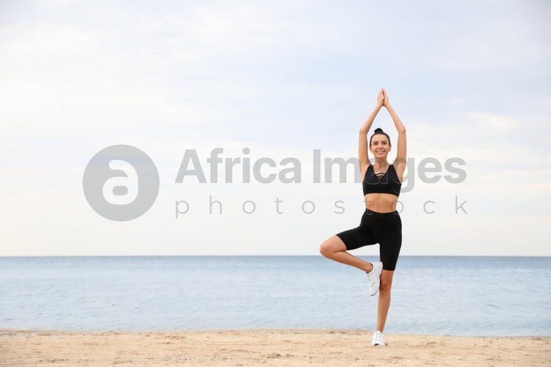 Young woman doing exercise on beach, space for text. Body training