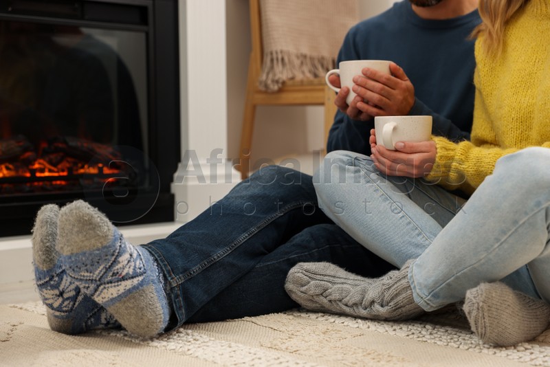 Photo of Lovely couple with hot drinks spending time together near fireplace at home, closeup