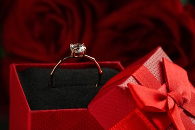 Beautiful engagement ring with gemstone in box against roses, closeup