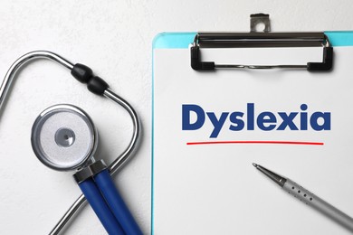 Image of Clipboard with word Dyslexia, pen and stethoscope on white table, flat lay