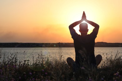 Man meditating near river at sunset, back view. Space for text