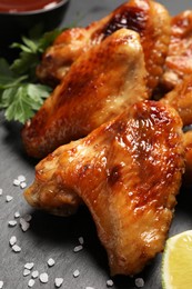 Photo of Delicious fried chicken wings and lime on black table, closeup
