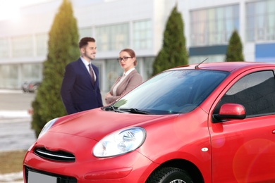 Customers buying car. Modern red auto and couple, focus on new auto