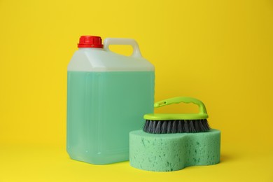 Canister of detergent, sponge and brush on yellow background. Cleaning supplies