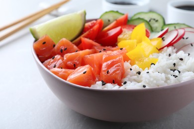 Delicious poke bowl with salmon, rice and vegetables on light grey table, closeup