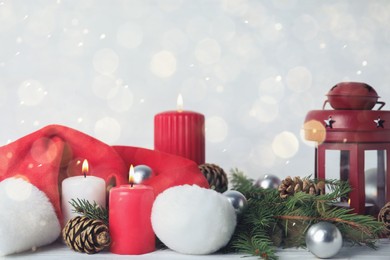 Photo of Burning candles and festive decor on table against light background, bokeh effect. Christmas eve