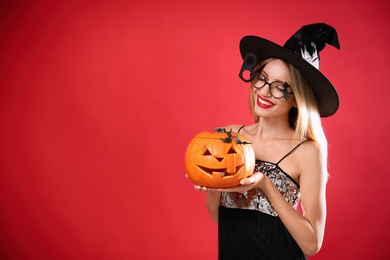 Beautiful woman in witch costume with jack o'lantern on red background, space for text. Halloween party