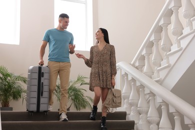 Happy couple with suitcase going down stairs in hotel