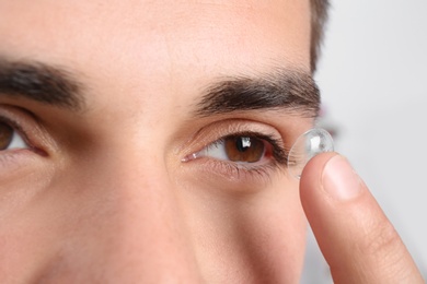 Young man putting contact lens into his eye, closeup