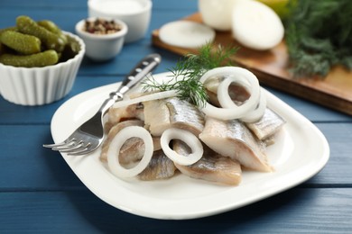 Photo of Plate with sliced salted herring fillet, onion rings and dill on blue wooden table, closeup