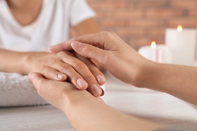 Cosmetologist massaging woman's hand at table in spa salon, closeup