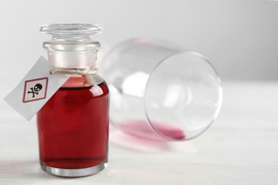 Bottle of poison and partially emptied glass on light background, closeup. Space for text