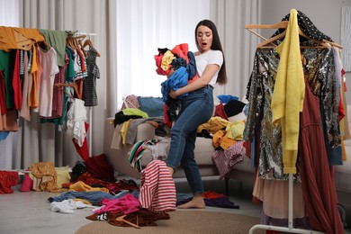Upset young woman with lots of clothes in room. Fast fashion