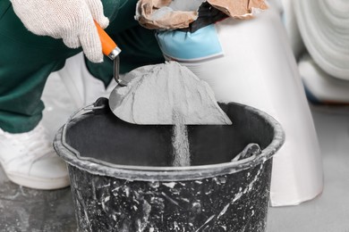 Photo of Worker with cement powder and trowel mixing concrete in bucket indoors, closeup