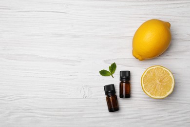Bottles of citrus essential oil and fresh lemons on white wooden table, flat lay. Space for text