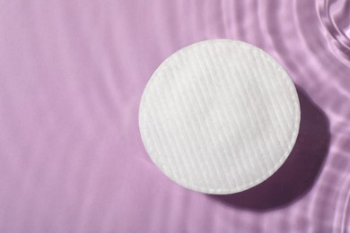 Cotton pad and micellar water on violet background, top view. Space for text