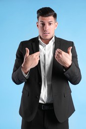 Emotional man in suit pointing at himself on light blue background