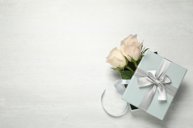 Elegant gift box with beautiful flowers on white table, top view. Space for text