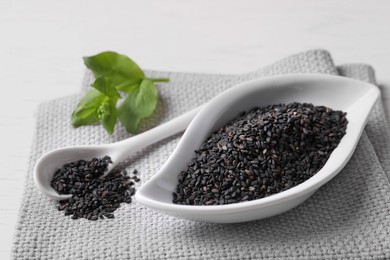 Photo of Black sesame seeds and green leaf on white table, closeup