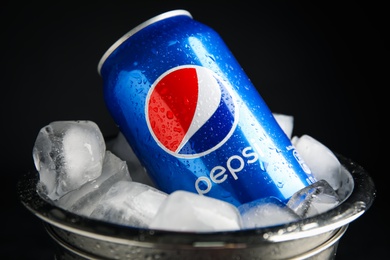 MYKOLAIV, UKRAINE - FEBRUARY 11, 2021: Can of Pepsi and ice cubes in bucket on black background, closeup