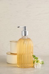 Photo of Stylish soap dispenser, flower and jars on light table