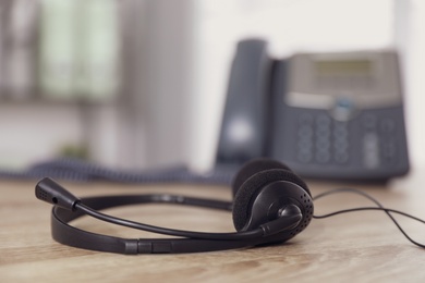 Headset on wooden table in office, closeup with space for text. Hotline service