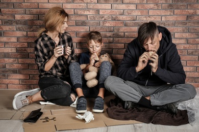 Poor homeless family sitting on floor near brick wall