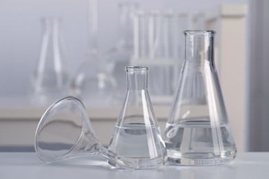 Conical flasks with transparent liquid and funnel on table in laboratory